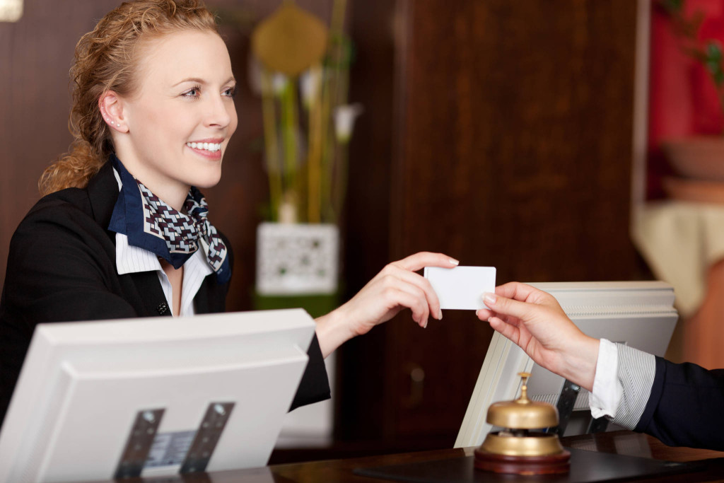 Smiling stylish beautiful receptionist handing over a blank white card to a client at the reception desk